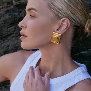 Woman wearing gold square earrings with a blurred natural background