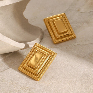 Pair of gold rectangular earrings on a beige surface