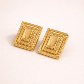 Pair of gold rectangular earrings on a light pink background