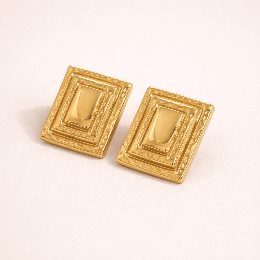 Pair of gold rectangular earrings on a light pink background