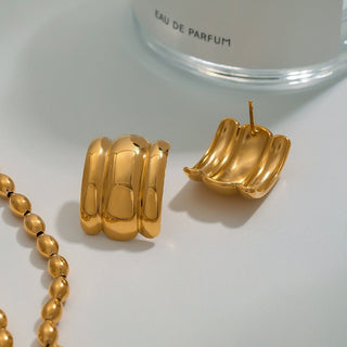 Gold hoop earrings and necklace on a white surface with a clear glass container labeled 'EAU DE PARFUM'.