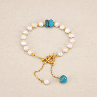 A beaded bracelet featuring white baroque pearls, two turquoise blue beads, and gold-toned metal hardware with a toggle clasp and dangling chain.
