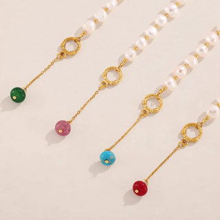 Four pearl necklaces with gold chain dangles and colorful bead charms in green, pink, blue, and red, arranged diagonally on a light beige background.